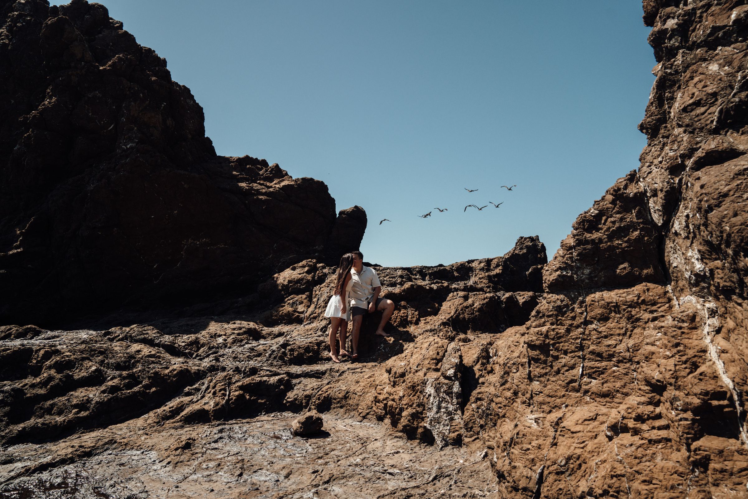 Pareja de pie entre las rocas de una caleta en la costa del Pacífico