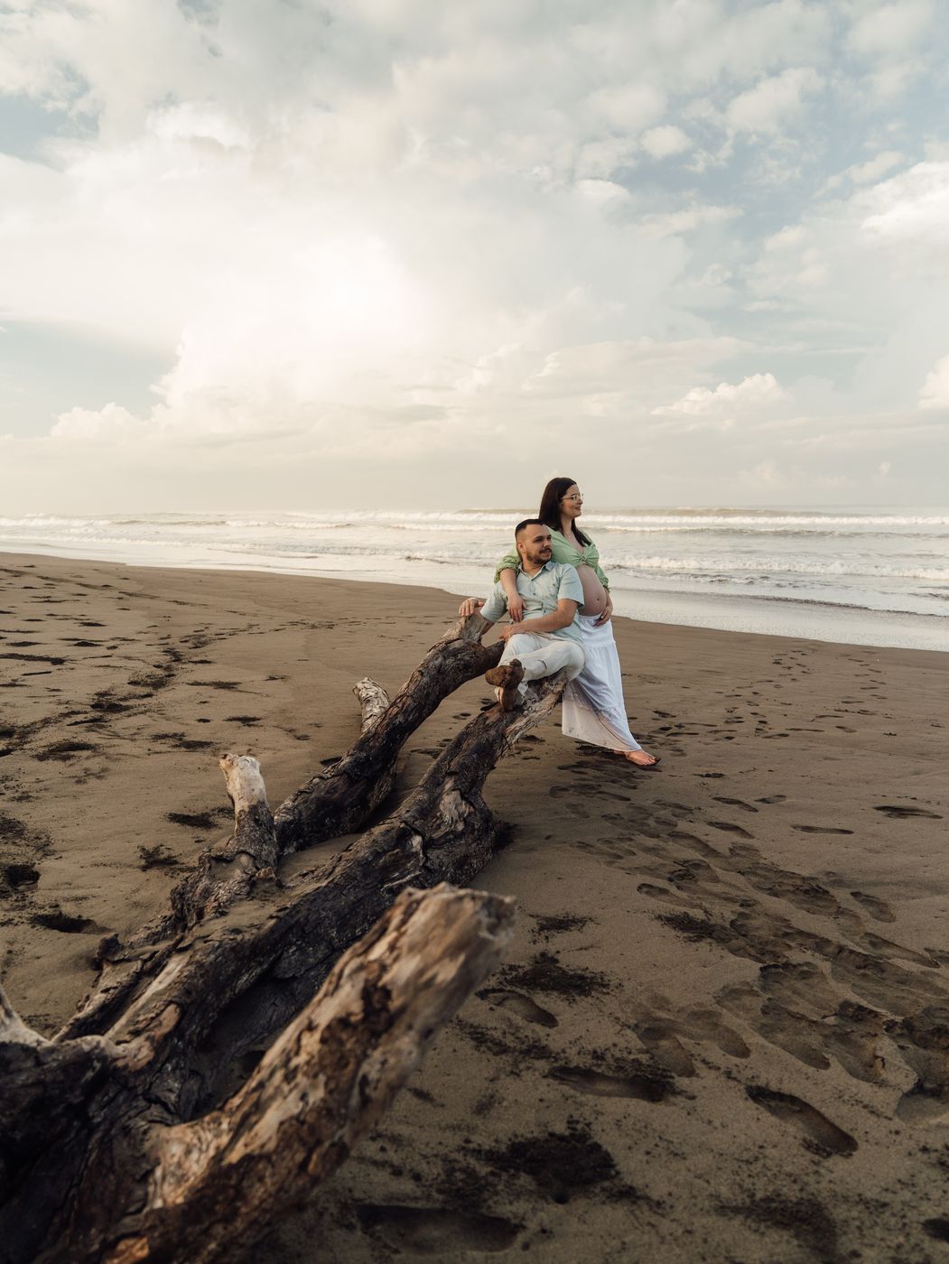 Pareja sentada sobre un tronco en la playa al atardecer
