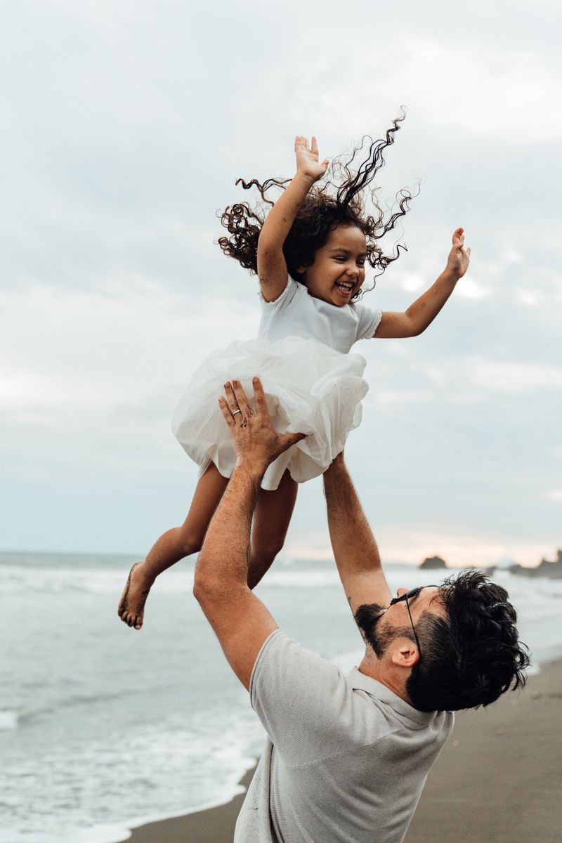 Papá lanzando a su hija al aire junto al mar
